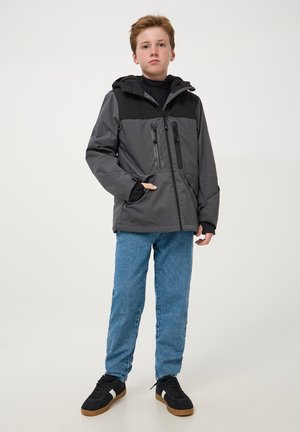 Szara i czarna kurtka z kapturem z zamykanymi kieszeniami, kontrastującą górną częścią oraz luźnym krojem, noszona z niebieskimi dżinsami i czarnymi sneakersami.