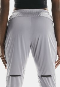 Pantalones deportivos gris claro hechos de una tela suave y elástica, con una cinturilla elástica ancha y detalles negros cerca de la rodilla.