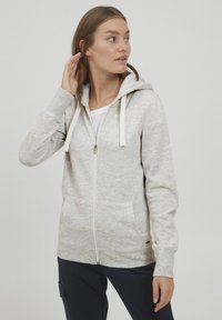 Helle graue Zip-Hoodie aus weichem, strukturiertem Stoff, mit Kapuze, Fronttaschen und kontrastierenden weißen Kordeln.