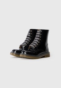 Bottines en cuir verni noir avec un design de laçage argenté, œillets dorés et semelle en caoutchouc texturé. Fini lisse avec un aspect brillant.