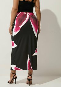 Svart maxiklänning med stort rosa blommönster, slät tyg, sidoflik och figurnära midja. Bärs med svarta högklackade sandaler.