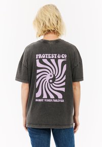 Donkergrijze oversized t-shirt met korte mouwen, voorzien van een grote roze spiraalafbeelding, tekst "PROTEST & CO" en "SUNNY VIBES FOREVER" op de achterkant.