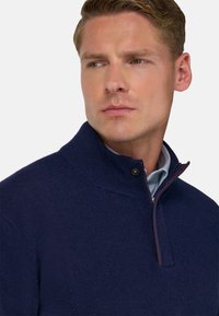 Marineblauer Pullover mit hohem Kragen und teilweisem Reißverschluss. Weiches Material mit einer Knopfdetaillierung am Hals.