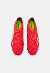 Red athletic shoes with textured synthetic upper, black and white accents, and bright green insoles. Features thin laces and streamlined design.