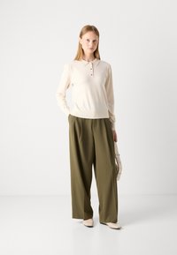 Lys beige pullover med krave og tre knaplukninger, parret med olivengrønne brede bukser og cremefarvede flade sko. Simpelt design, glat tekstur.