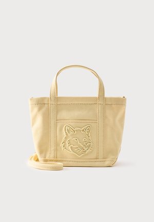 Sac fourre-tout en toile beige avec des poignées courtes, une bandoulière amovible et une tête de renard brodée sur la poche avant.