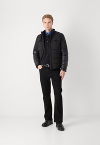 Black puffer jacket with a hood and glossy sleeves, paired with a dark polo shirt, black trousers, and black boots. Simple, fitted design.