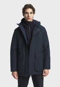 Námornícky modrá nepremokavá bunda s kapucňou, s dvoma prednými vreckami a zipsovým uzáverom. Hladká textúra a moderný dizajn.
