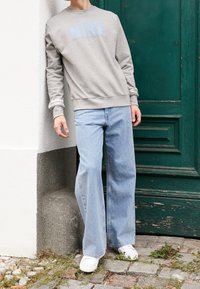 Gray sweatshirt with light blue "NIKE" logo, paired with light blue wide-leg jeans and white sneakers, leaning against a green door.