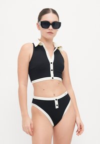 Black two-piece swimsuit featuring a collared crop top with button accents and high-waisted bottoms, detailed with white trim.