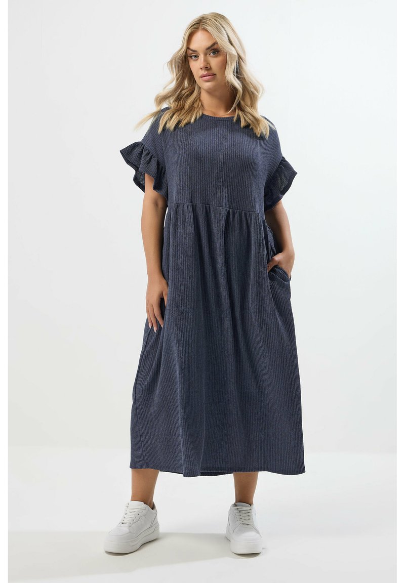 Dunkelblau gestreifte Maxikleid mit rundem Ausschnitt, kurzen Rüschärmeln und seitlichen Taschen. Kombiniert mit weißen Sneakers.