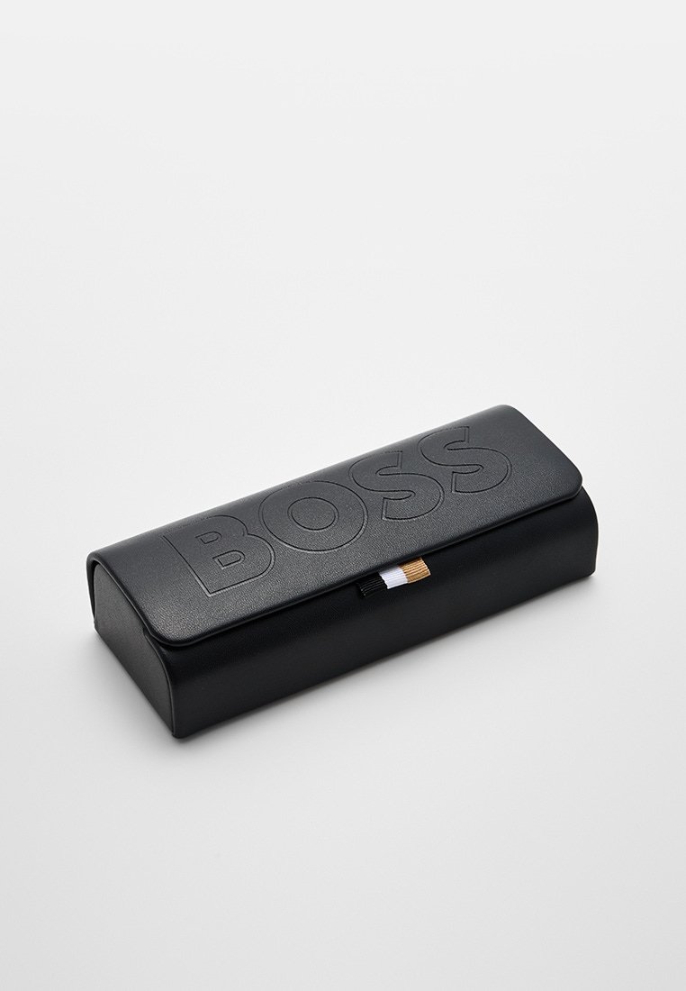 Astuccio in pelle nera a forma di matita con il logo "BOSS" in rilievo, forma rettangolare, texture liscia e un piccolo etichetta colorata su un lato.
