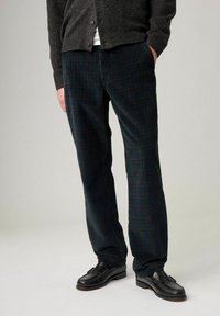Pantaloni in velluto a coste verde scuro con righe verticali, caratterizzati da una vestibilità rilassata e abbinati a mocassini in pelle nera.