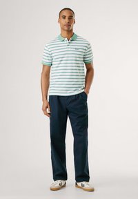 Črtasta polo majica v beli in mint zeleni barvi s zelenim ovratnikom, oblečena s temno modrimi hlačami in belimi supergami s črnimi detajli.