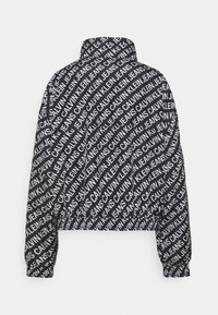 Sort jakke med høj krave og elastiske manchetter, helt dækket af et diagonalt hvidt mønster med teksten "CALVIN KLEIN JEANS".