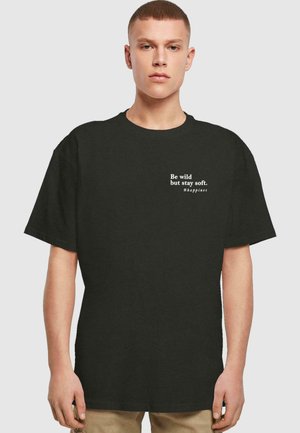 Sort bomulds t-shirt med en afslappet pasform. Hvid tekst på forsiden siger "Vær vild, men forbliv blød. #lykke." Minimalistisk design.