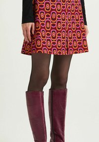 Una gonna a-line multicolore presenta audaci motivi geometrici in rosa, arancione e viola. Abbinata a stivali testurizzati bordeaux al ginocchio.