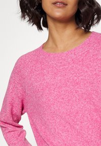 Rosa gestrickter Pullover mit rundem Halsausschnitt und langen Ärmeln, der eine weiche Textur und eine leicht lockere Passform bietet.