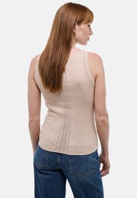 Débardeur beige clair à coupe ajustée, présentant des détails en tricot vertical délicat dans le dos, associé à un jean bleu taille haute.
