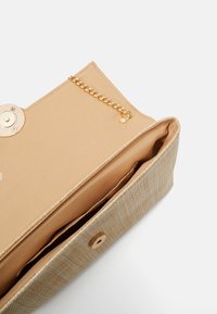Béžová psaníčko s texturovaným tkaným designem, zlatými prvky, magnetickým uzávěrem a vnitřním řetězovým úchytem. Uvnitř hladká textilní podšívka.