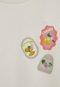 Kolme värikästä hedelmätarraa valkoisella kankaalla: appelsiinit, sitruunat ja tuoreet rypäleet, joissa on vastaavat kuvitukset ja tekstit.