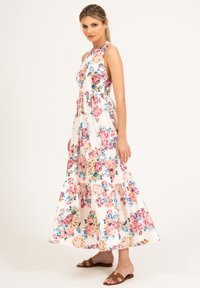 Kwiatowa sukienka maxi w kolorze białym z różowymi i niebieskimi kwiatami. Posiada dekolt halter, warstwowy dół i luźny krój. Noszona z brązowymi sandałami.