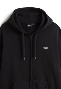 Černá mikina s kapucí na zip z měkké tkaniny, vybavená předním zipem, kapucí se šňůrkami a malým bílým logem Vans na levé straně hrudi.