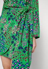 Zielona sukienka z kwiatowym i zwierzęcym wzorem w odcieniach różu, fioletu i granatu. Miękka tkanina z węzłowym detalem w talii, długość do połowy uda.