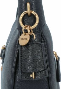 Borsa nera testurizzata con hardware dorato, etichetta con logo pendente e tasca laterale con zip e flap decorativo.