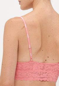 Rosa blonde bh med justerbare stropper som har "HUGO" merke. Bølgeformede kanter og teksturert stoff med blomsterdesign.