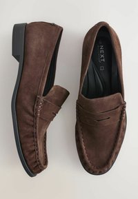 Mocassins en cuir suédé marron avec une accentuation cousue et une semelle en caoutchouc noir basse, dotés d'un bout arrondi et d'un design à enfiler.