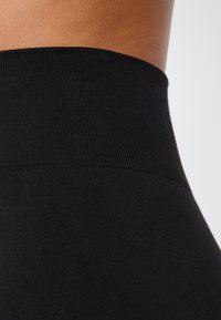 Leggings noirs taille haute avec une texture côtelée et une finition lisse, dotés d'une taille élastique, conçus pour une silhouette ajustée.