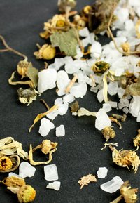 Gedroogde bloemen en kleine, witte kristallen verspreid over een donkere ondergrond, met aardse tinten en verschillende texturen van de botanische elementen.