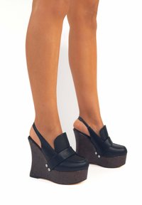 Sandali wedge neri in pelle con una fascia frontale e design slingback, dotati di un tacco a cuneo testurizzato simile al sughero e dettagli argentati.