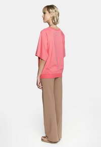 Różowy, oversize'owy t-shirt z raglanowymi rękawami i ściągaczem na dole, zestawiony z luźnymi brązowymi spodniami. Gładki materiał i luźny fason.