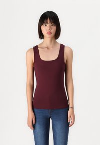 Débardeur ajusté bordeaux avec un décolleté carré, sans manches et en tissu lisse. Assorti à un jean bleu. Style simple et minimaliste.
