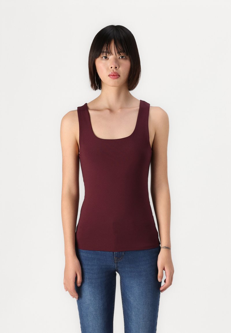 Débardeur ajusté bordeaux avec un décolleté carré, sans manches et en tissu lisse. Assorti à un jean bleu. Style simple et minimaliste.