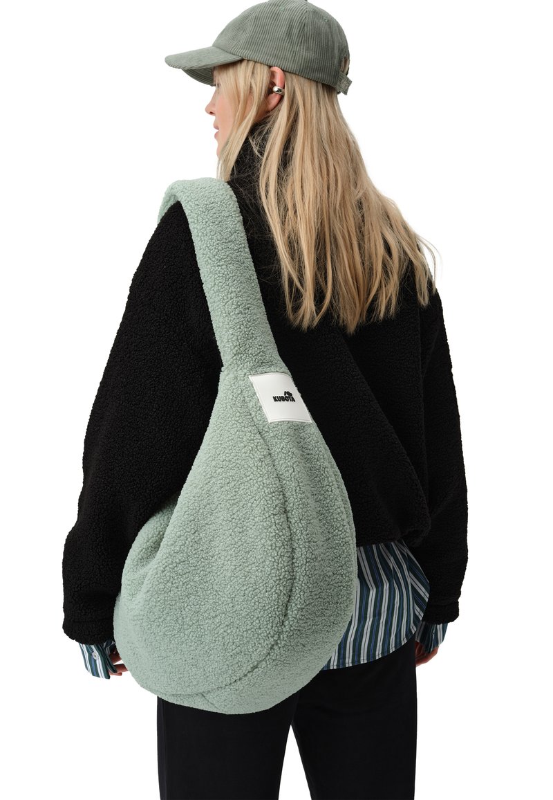 Zielona torba typu hobo z pluszowego materiału o miękkiej teksturze, w oversize'owym kształcie, z regulowanym paskiem, z małą białą metką z przodu.