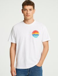 White cotton t-shirt featuring a circular graphic on the chest with a sunset design in red, orange, yellow, and blue wave patterns.