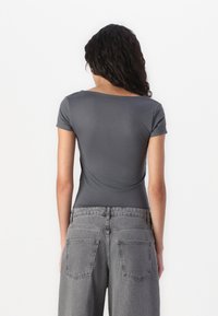 T-shirt gris ajusté à manches courtes et à encolure dégagée, associé à un jean gris taille haute avec poches arrière et coupe décontractée.