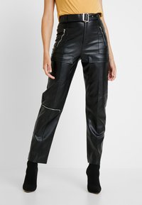 Black faux leather trousers with a high waist, zipper accents, large pockets, and a belt. Smooth texture and tailored fit.