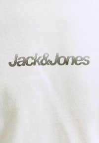Μαύρο κείμενο "Jack & Jones" εκτυπωμένο σε λευκό ύφασμα, κεντραρισμένο και καθαρό, που δείχνει το λογότυπο της μάρκας σε ένα ένδυμα.