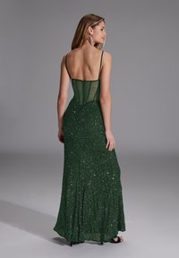 Vestito da sera verde con corpetto aderente e pannelli trasparenti, gonna svasata con paillettes e spalline sottili. Design senza schiena.