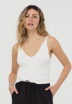 Top in cotone bianco a coste con scollatura a V profonda e spalline sottili, abbinato a pantaloni neri con lacci. Tessuto liscio e design aderente.
