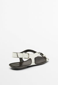 White and black leather sandal with adjustable ankle strap, flat sole, open toe design, and silver buckle detail.