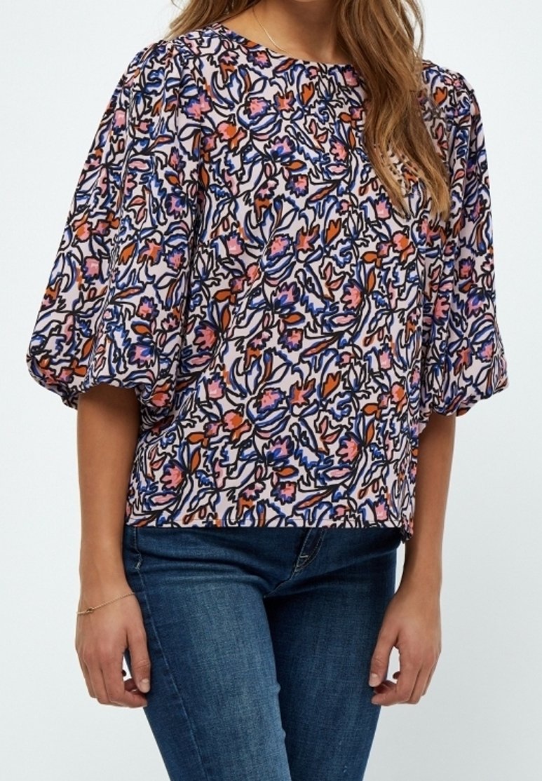 Top con stampa floreale e maniche a sbuffo. Presenta motivi vibranti in rosa, blu e arancione su uno sfondo chiaro. Realizzato in tessuto morbido e leggero.