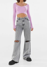 Light pink ribbed long-sleeve crop top paired with gray ripped wide-leg jeans. The outfit features distinct patterns and a relaxed fit.