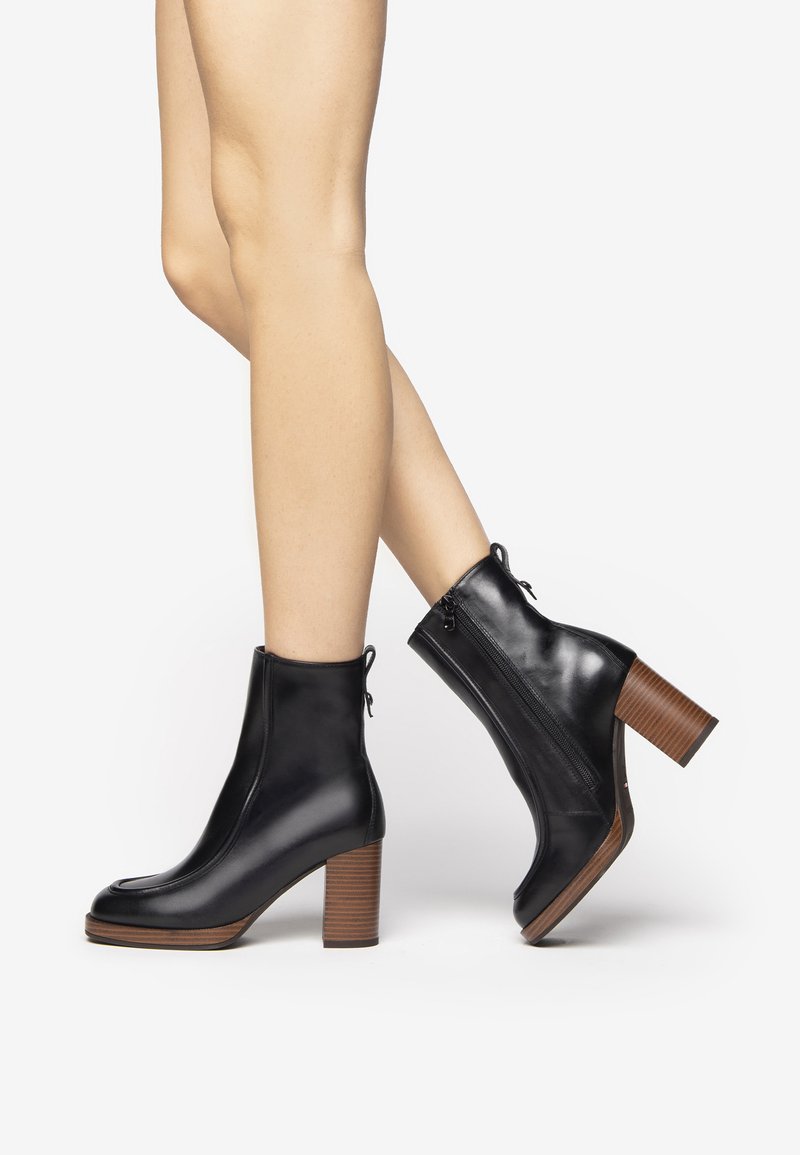 Black leather ankle boots with a round toe and a chunky brown heel. Features a side zipper and textured heel accent.