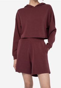 Sweat à capuche bordeaux avec un design court, des manches larges et une poche avant, associé à un short bordeaux assorti avec des poches latérales.