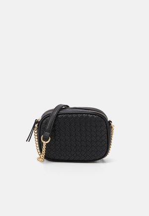 Sort vævet crossbody-taske med guldkæde-rem og lynlåslukning, kompakt rektangulær form mod ensfarvet baggrund.